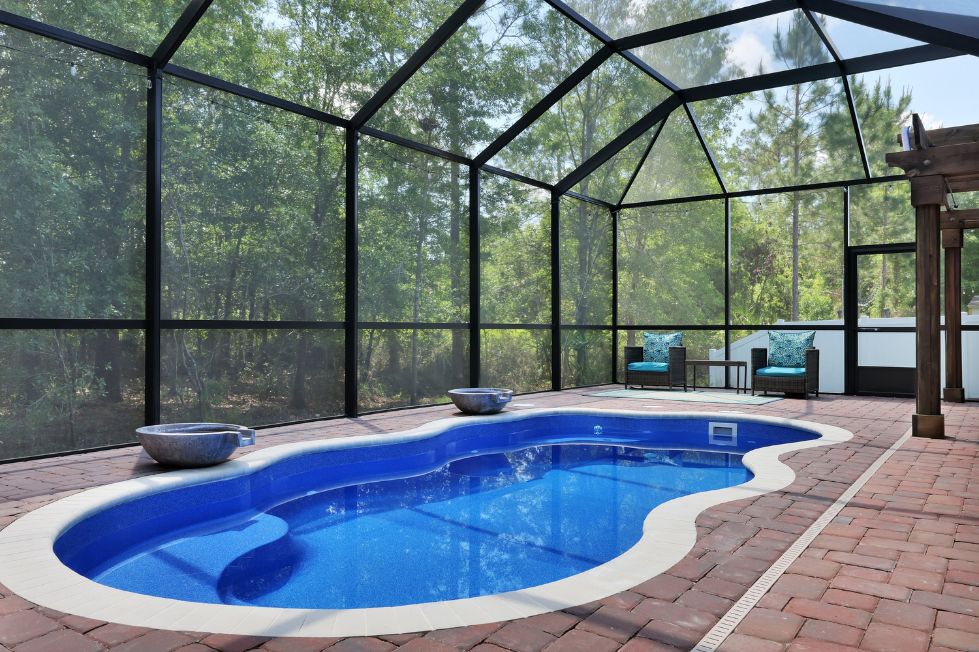 Freeform fiberglass pool inside a screened lanai with paver deck