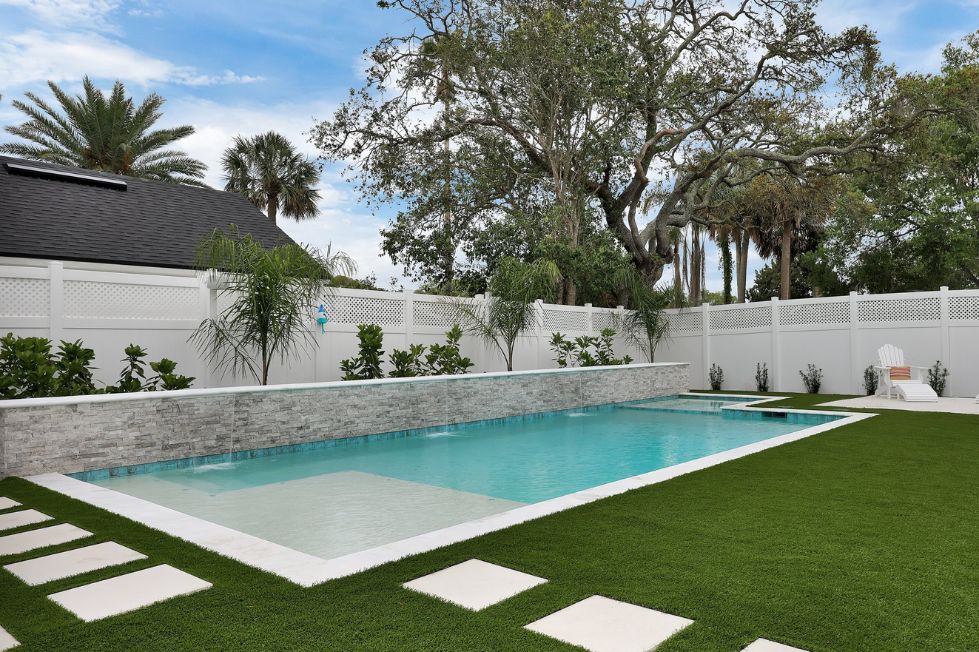 Modern rectangular swimming pool with artificial turf and white privacy fence
