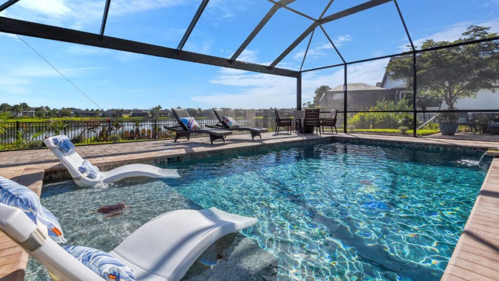 Screen-enclosed backyard pool with tanning ledge, lounge chairs, and lake view 