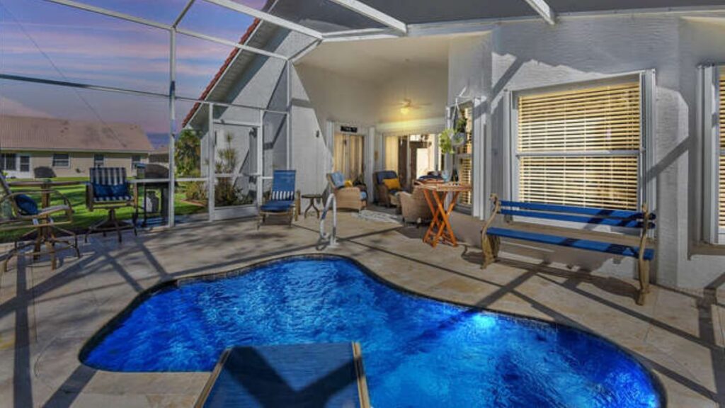Freeform backyard pool under a screened enclosure beside a covered patio at dusk 
