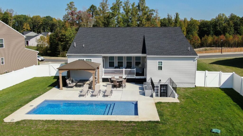 Aerial view of a backyard pool with pergola, patio seating, screened porch, and fenced lawn