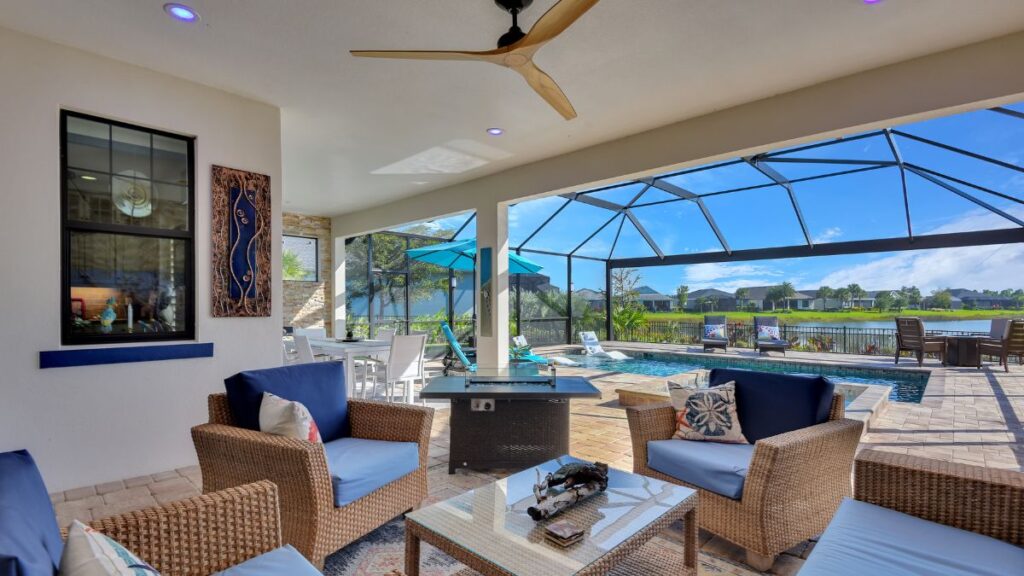 Covered patio with wicker seating overlooking a screened pool, spa, and lake view 