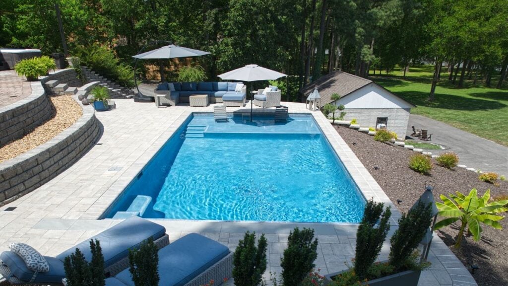Terraced backyard pool with stone patio, tanning ledge, lounge seating, and a pool house