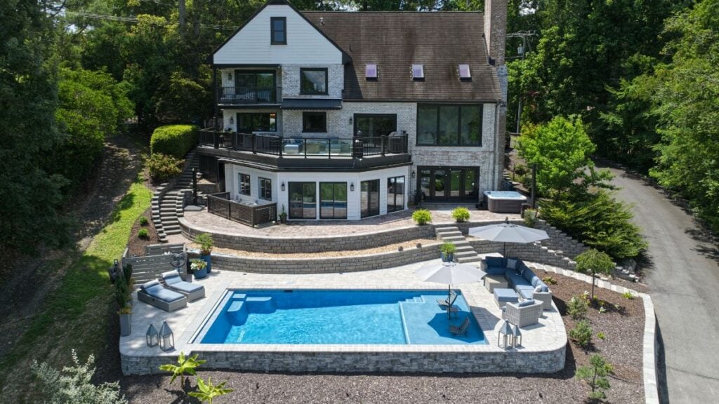 Aerial view of a multi-level stone home with terraced patios, hot tub, and a raised backyard pool