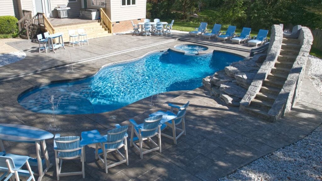 Freeform pool with rock waterfall, stone steps, blue patio furniture, and a stamped concrete patio