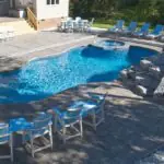 Freeform pool with rock waterfall, stone steps, blue patio furniture, and a stamped concrete patio