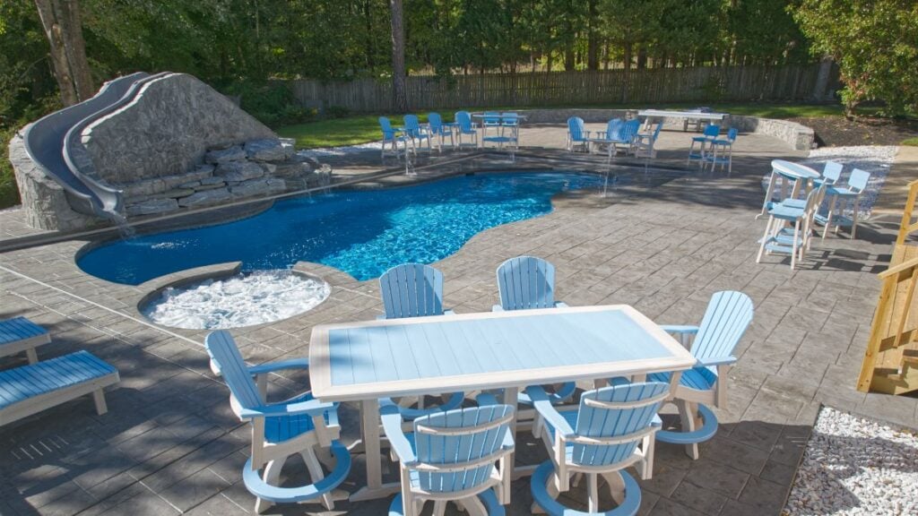 Freeform pool with a rock waterslide, spa, and blue patio dining set on a stamped concrete deck