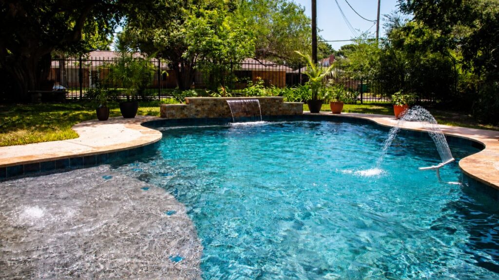 Freeform swimming pool with a Baja shelf, raised waterfall, and deck jet fountain