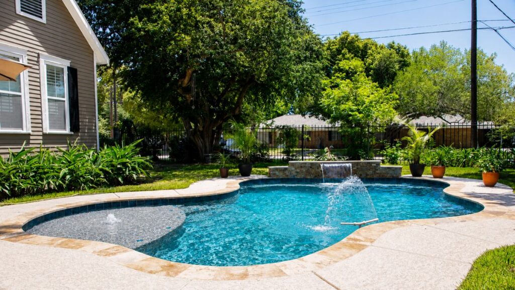 Freeform swimming pool with a sheer descent waterfall, tanning ledge, and deck jet