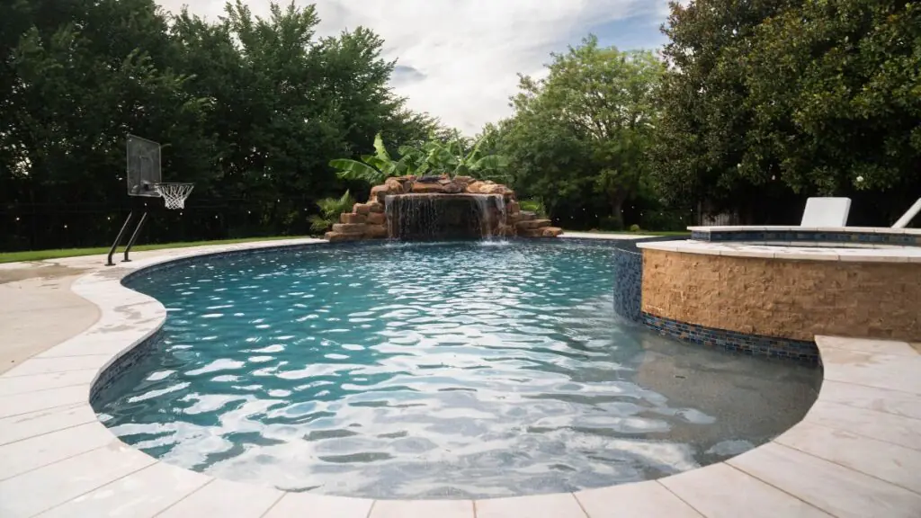 Freeform swimming pool with a raised spa, rock waterfall, and built-in basketball hoop