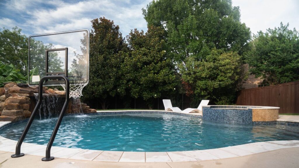Backyard swimming pool with a swim-up spa, basketball hoop, and lounge chairs