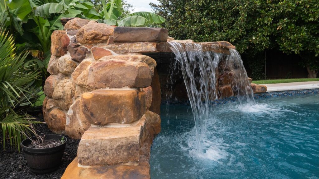 Natural rock waterfall cascading into a freeform swimming pool with tropical landscaping