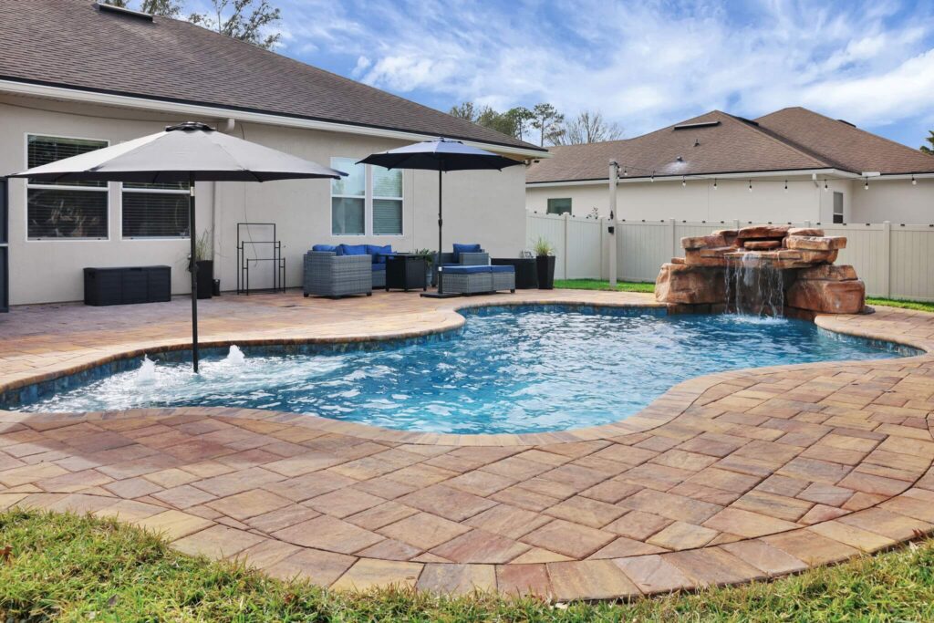 Freeform inground pool with rock waterfall, paver patio, and outdoor seating