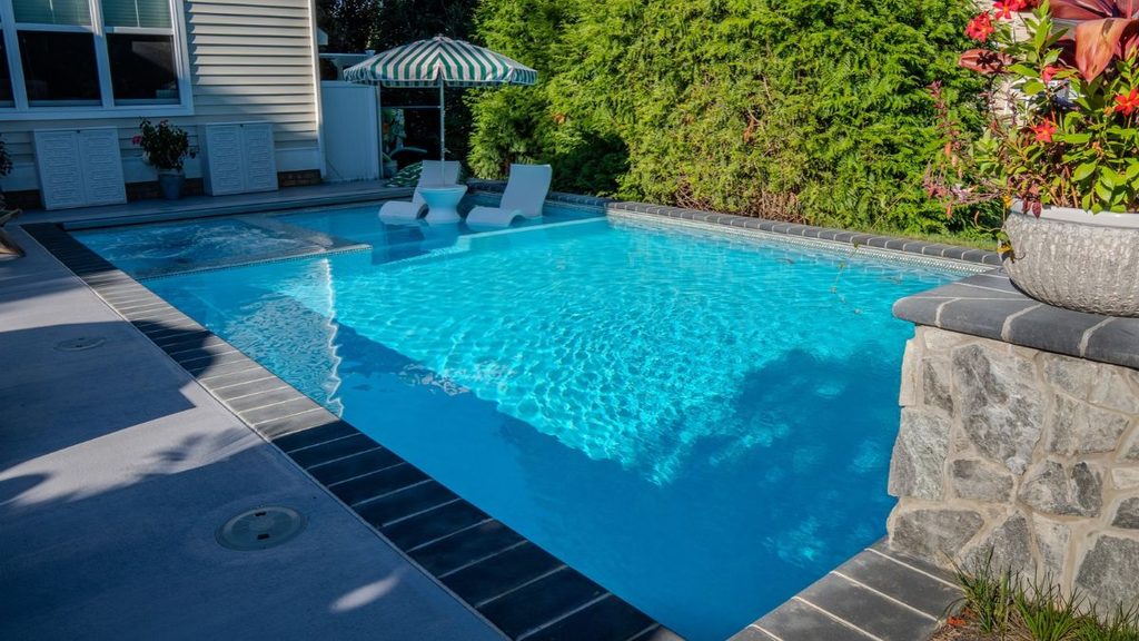 Inground pool with shallow tanning ledge, in-pool loungers, and stone coping