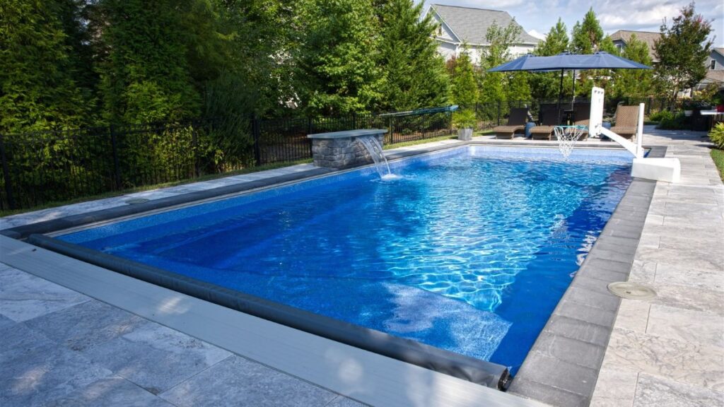 Rectangular inground pool with stone coping, water feature, basketball hoop, and spacious pool deck