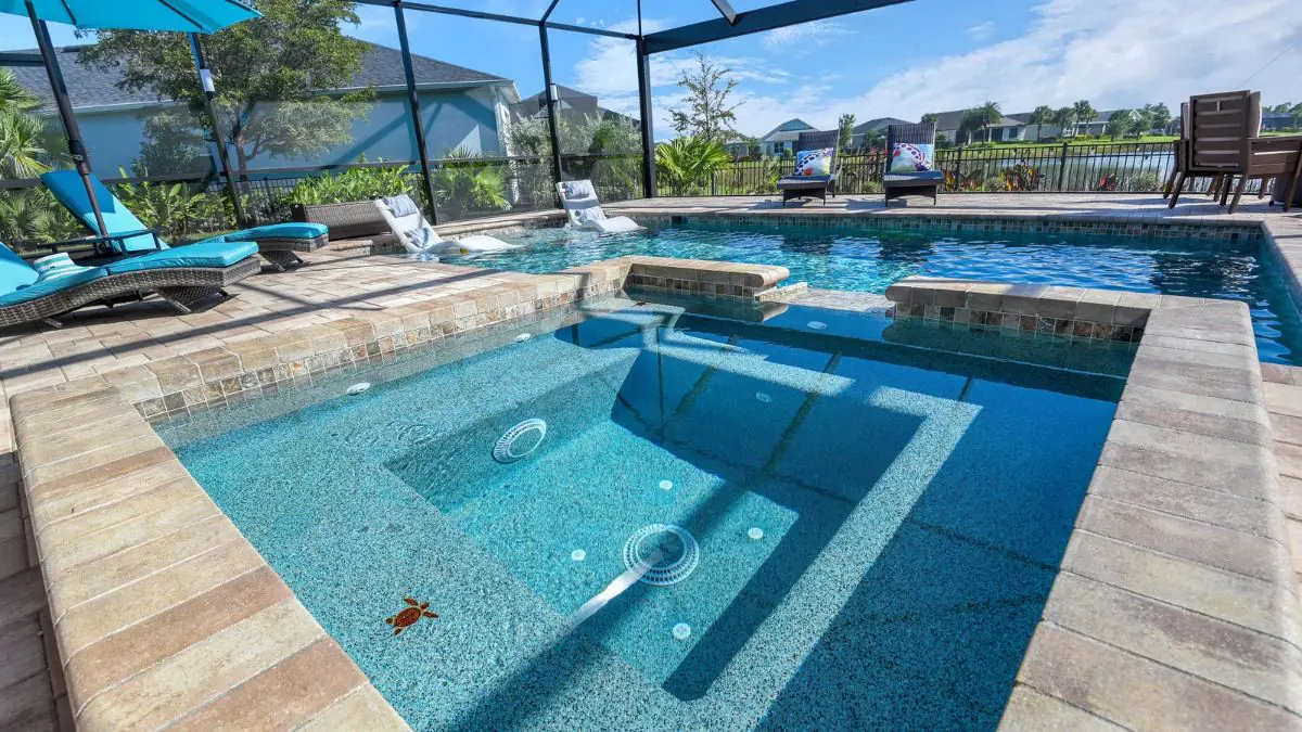 Inground pool with raised spa, poolside loungers, and screened enclosure