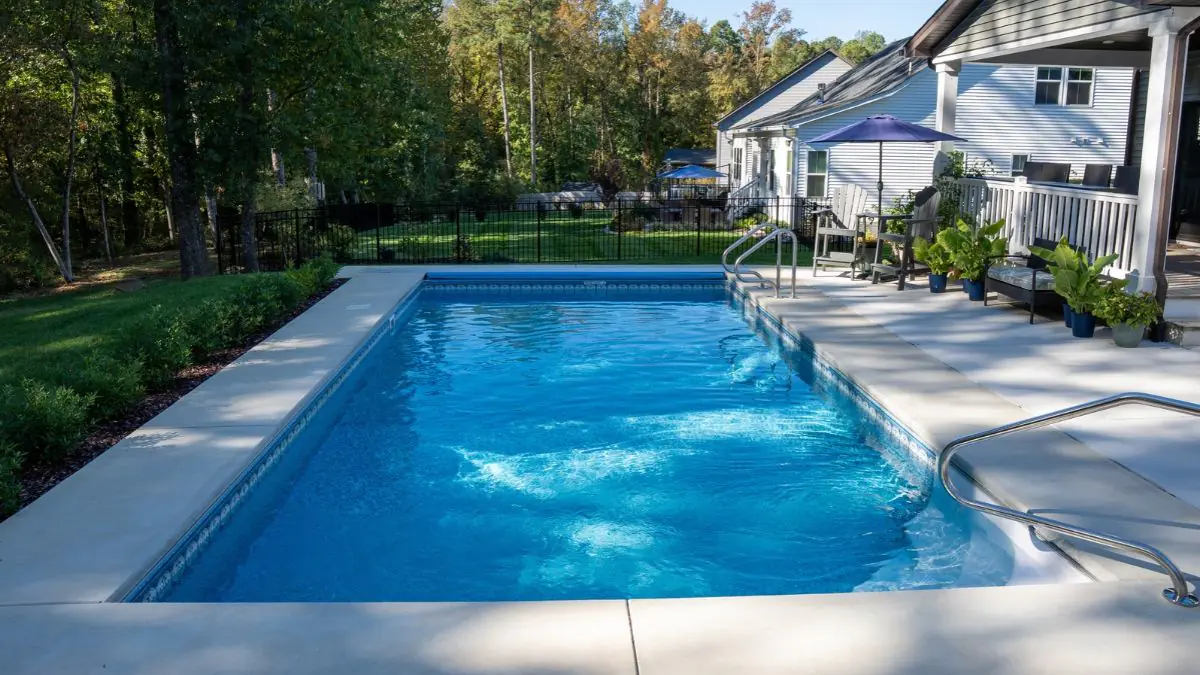 Inground pool with wide concrete deck, metal handrails, and backyard seating