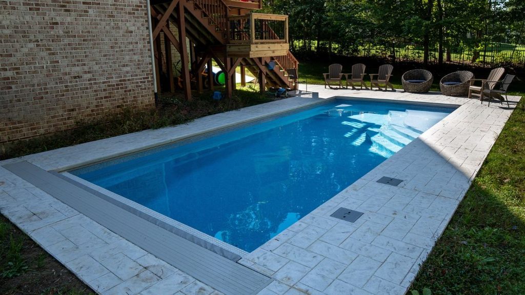 Inground pool with stone patio, wide steps, and backyard seating area