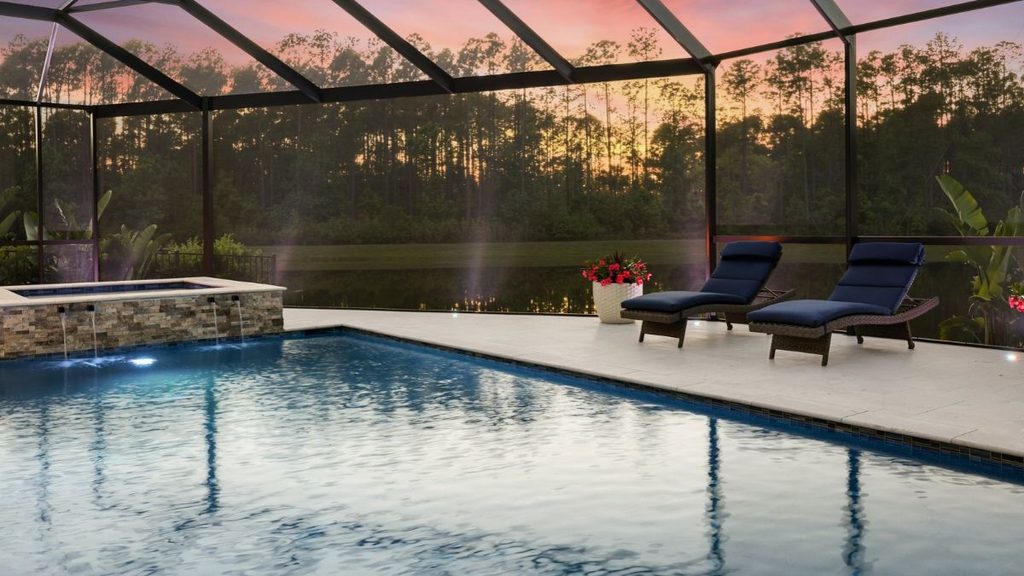 Inground pool with raised spa, screened enclosure, and poolside loungers at sunset