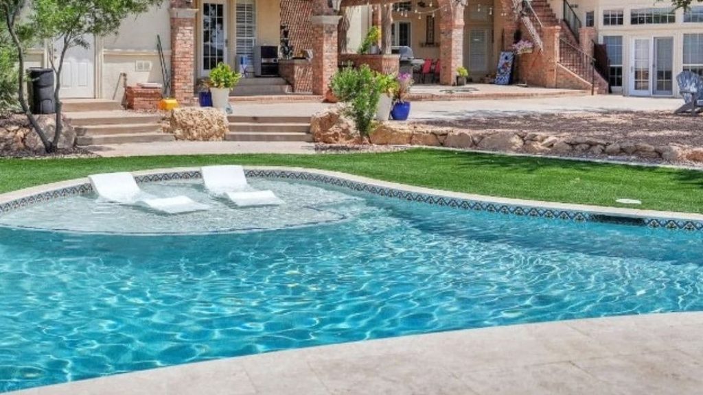 Backyard pool with a raised stacked-stone spa, bubbling jets, colorful patio umbrellas, lounge chairs, and a travertine paver patio