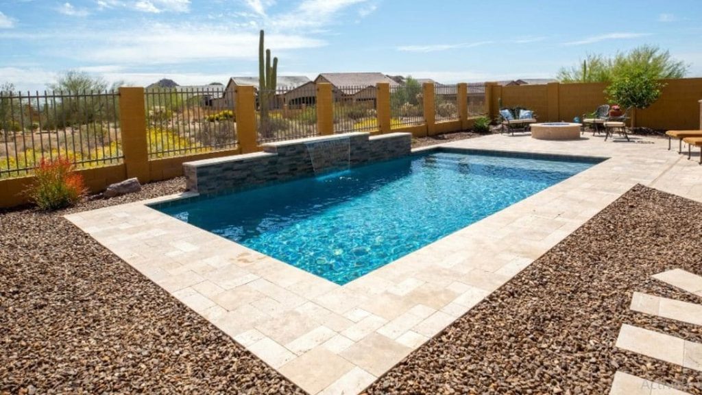 Rectangular backyard pool with a stacked stone waterfall, travertine deck, gravel landscaping, and a fire pit in a desert setting