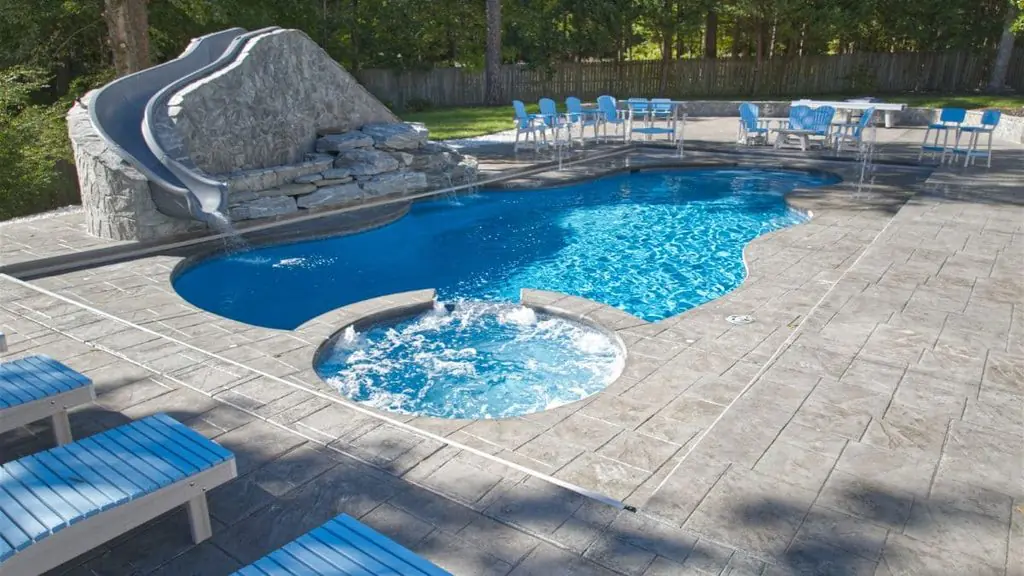 Freeform backyard pool with a rock slide and waterfall, a round spa with bubbling jets, stamped concrete deck, and blue lounge and Adirondack chairs