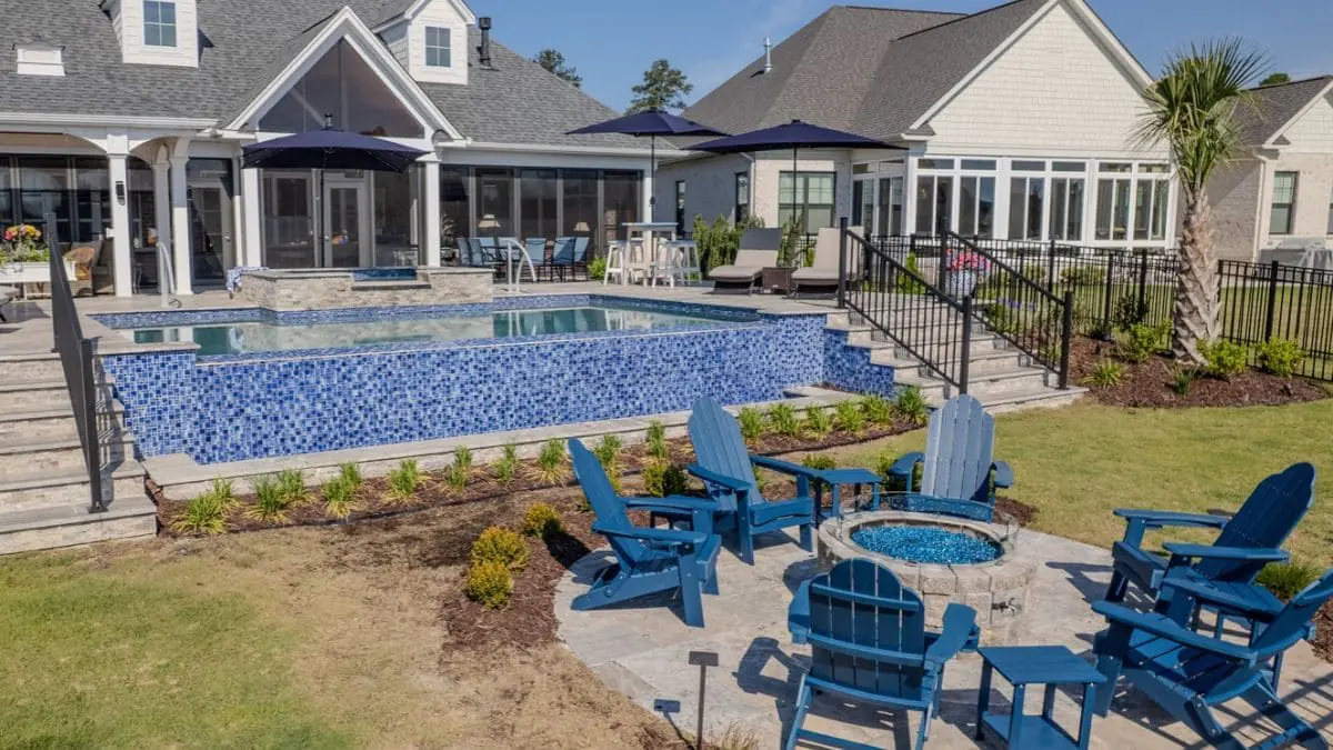 Raised backyard pool with a blue glass tile wall, attached spa, stone steps, and a fire pit surrounded by blue Adirondack chairs