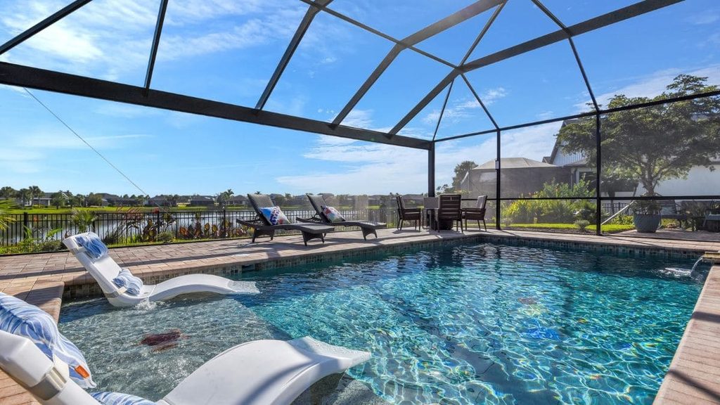Screened-in backyard pool with a tanning ledge and in-pool lounge chairs, brick paver deck, outdoor seating, and a lake view in the background